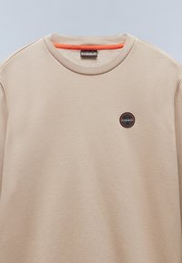 Felpa beige con collo rotondo e interno arancione. Presenta un piccolo logo circolare sul petto e una texture liscia.