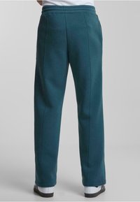 Pantalones de chándal verde azulado hechos de una tela suave, con un corte relajado, cintura elástica y costuras laterales sin bolsillos visibles.