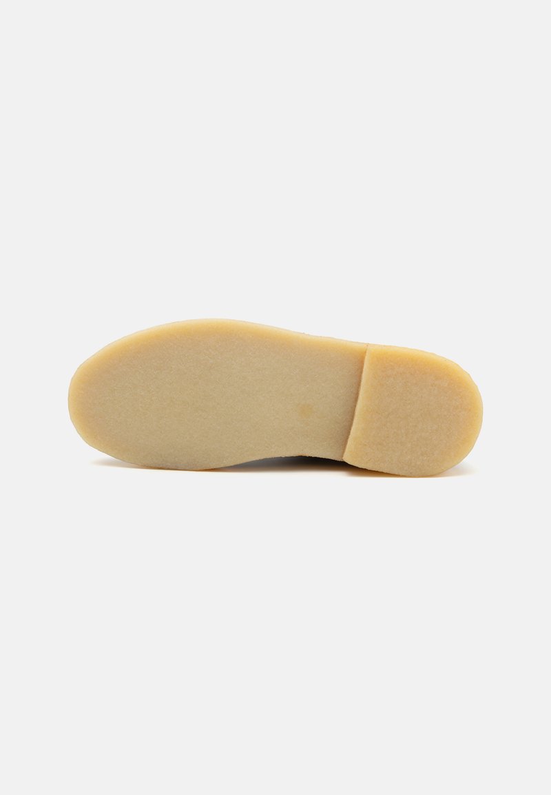Suola di una scarpa, materiale gommoso, colore beige, forma arrotondata, texture liscia, con leggera spessore al tallone per stabilità.