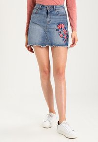 Jupe en denim avec un ourlet effiloché, ornée d'une broderie florale sur le côté gauche. Design classique avec cinq poches et fermeture à boutons sur le devant.