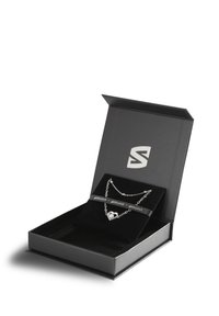 Silver necklace with heart pendant displayed in a black gift box lined with black velvet. Box features a logo on the interior.