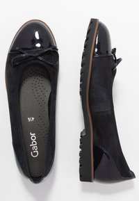 Damskie granatowe mokasyny ze zamszu i lakierowanej skóry, z teksturowanymi czarnymi gumowymi podeszwami oraz małą ozdobną kokardką z przodu.