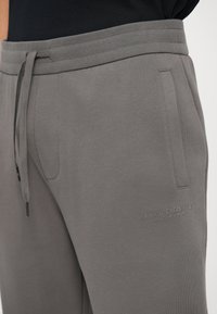 Graue Jogginghose mit elastischem Bund, Seitentaschen und geprägtem Logodesign. Hergestellt aus weichem Material mit glatter Textur.