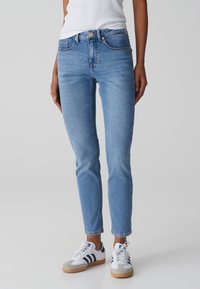Jeans ajustados de color azul claro hechos de denim con un diseño clásico de cinco bolsillos, cierre de botón y detalles de costura en contraste. Combinados con zapatillas blancas.