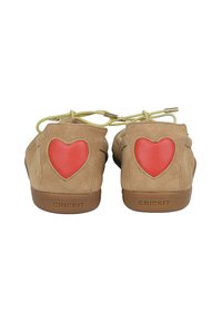 Chaussures en daim de couleur beige clair avec des accents en forme de cœur orange et des lacets verts. Présente un branding sur les semelles en caoutchouc. Design arrondi avec une texture douce.