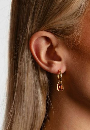 Goldener Creolen-Ohrring mit einem rechteckigen roten Edelstein-Anhänger, der eine polierte Oberfläche und ein sicheres Verschlusssystem zeigt, getragen nahe dem Ohr einer Person.