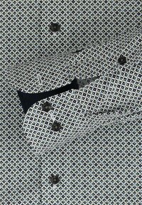 Koszula w wzory z diamentowym motywem w granatowym i jasnoniebieskim kolorze na białym tle, z czarnymi guzikami i kontrastującym wykończeniem mankietów.