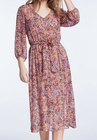 Blumenkleid in mittellanger Form aus leichtem, transparentem Stoff. Mit V-Ausschnitt, 3/4-Ärmeln, taillierter Taille mit Bindegürtel und lebendigen Mustern in Orange, Pink und Lila.