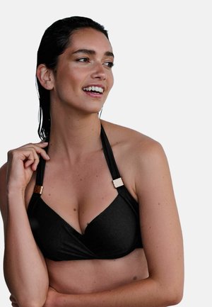 Mosolygó nő nedves hajjal, fekete pántos bikini felsőt viselve, egyik pántot tartja a kezével, oldalra néz.