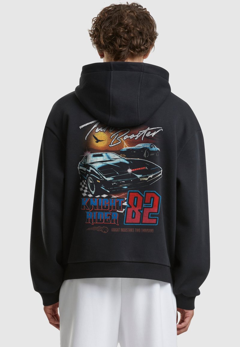 Personne portant un sweat à capuche noir avec un graphisme sur le thème Knight Rider avec des voitures, un soleil et le texte « Turbo Booster », « Knight Rider 82 » dans le dos.