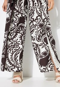Wijde broek met een zwart-wit bloemenpatroon, met zijsplitten. Gemaakt om te dragen met gevlochten beige blokhakken.