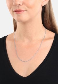 Collana di catena argentata indossata da una persona, caratterizzata da un motivo delicato e una superficie liscia, indossata su una maglietta nera a scollo a V.