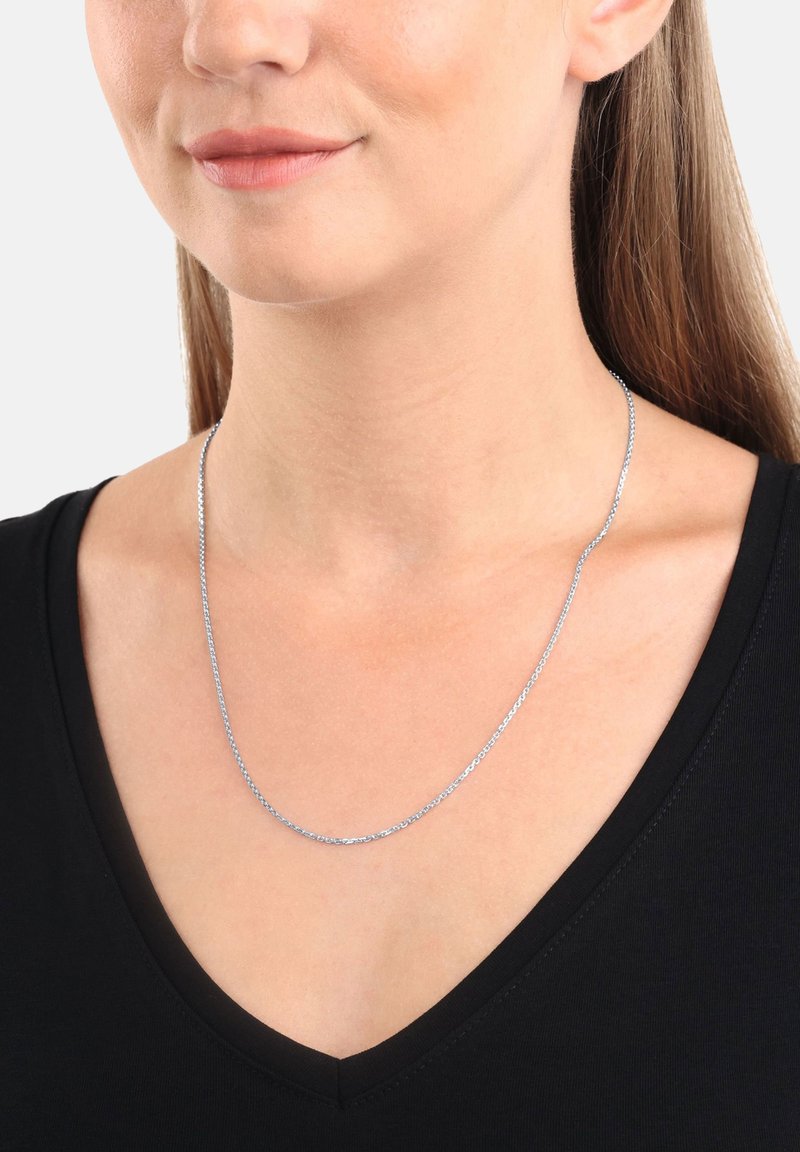 Collana di catena argentata indossata da una persona, caratterizzata da un motivo delicato e una superficie liscia, indossata su una maglietta nera a scollo a V.