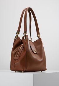 Brown leather handbag with a slouchy design, dual top handles, gold hardware accents, and a side zip pocket for added detail.