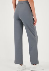 Gray wide-leg pants made of textured fabric with a high waistband, feature a smooth finish and are paired with white sneakers.