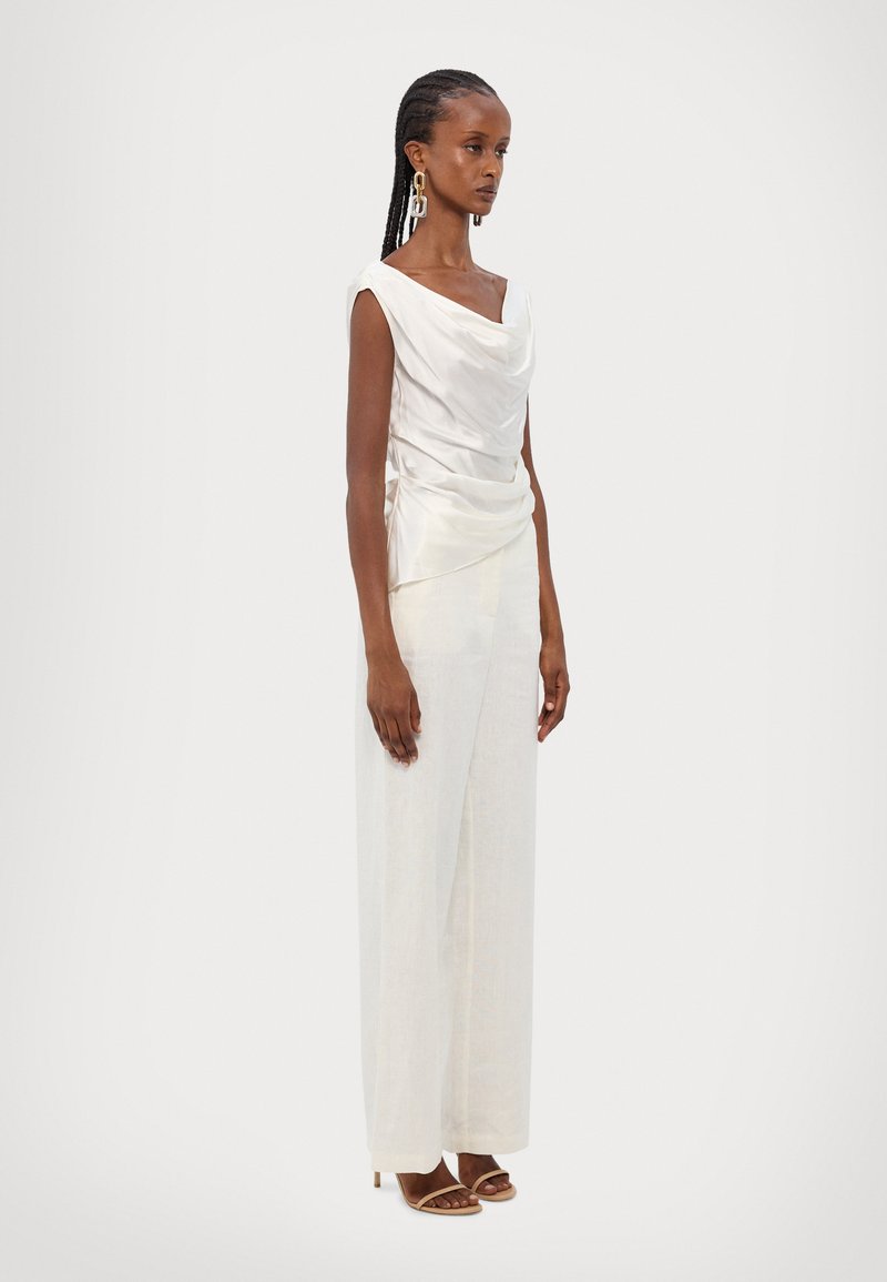 White draped satin top with cap sleeves paired with light linen trousers, featuring a loose fit and a smooth texture. Sleek heels complete the look.