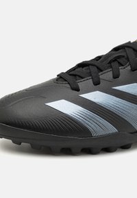 Crampons de football noirs avec une surface texturée, présentant trois rayures bleu clair, des lacets noirs et des crampons moulés pour une traction optimale.