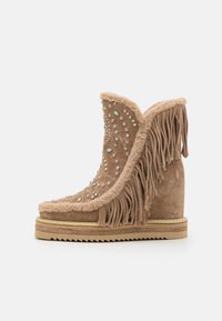 Bottine en suede beige à la cheville avec des détails en franges et ornée de strass, dotée d'un talon en wedge et d'une semelle texturée.