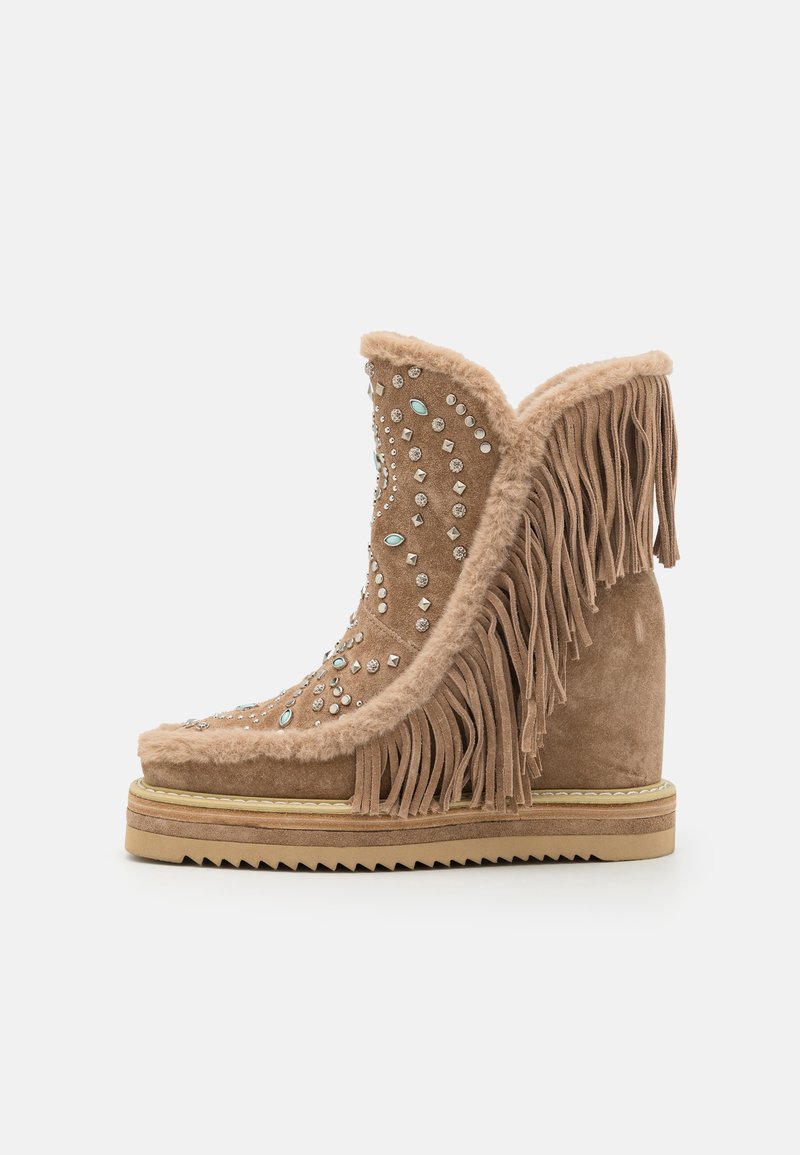 Bottine en suede beige à la cheville avec des détails en franges et ornée de strass, dotée d'un talon en wedge et d'une semelle texturée.