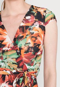 Kwiatowa sukienka w żywych odcieniach pomarańczowego, czerwonego i zielonego, z głębokim dekoltem w serek, krótkimi rękawami i wiązanym w pasie do regulacji. Gładka tekstura materiału.