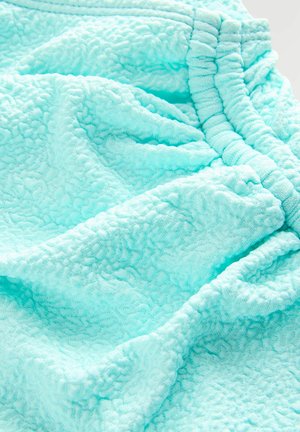 Țesătură texturată de culoare albastru deschis, cu o atingere moale și pufoasă, având cusături pliate pe margine, ceea ce creează un model subtil în valuri.