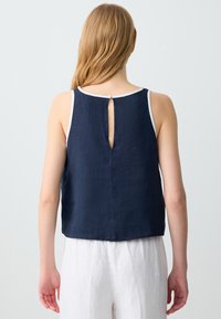Top senza maniche di colore blu navy con scollo rotondo, caratterizzato da un'apertura a chiave sul retro e rifiniture bianche lungo i bordi. Realizzato in un tessuto testurizzato.