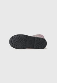Semelle de chaussure avec un dessous en caoutchouc noir à motif, présentant des rainures profondes pour une traction et une légère courbure vers l'arrière pour un soutien de la voûte.