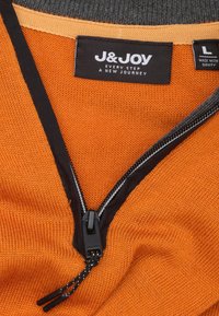 Zip-up kledingstuk in levendig oranje breiwerk met een zwarte rits en afwerking. Label geeft "J&Joy" aan, maat L. Zachte textuur met een ontspannen pasvorm.