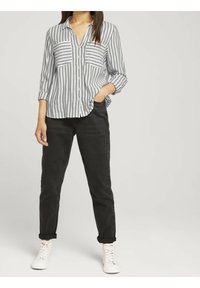 Gestreept button-up shirt in grijs en wit, met twee borstzakken. Gecombineerd met zwarte broek en witte veterschoenen.