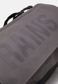 Grau wasserdichte Tasche mit großem, geprägtem "RAINS"-Schriftzug, schlankem Design, glatter Textur und schwarzen Akzenten am Boden.