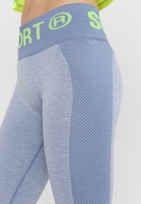 Jasnoniebieskie legginsy sportowe z teksturowanym, wplecionym paskiem w talii. Posiadają pionowe paski po bokach oraz gładki materiał na całej powierzchni.