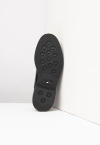Sort gummisål med cirkulært grebsmønster, buede kanter og præget mærkelogo. Robust, struktureret overflade for trækkraft.