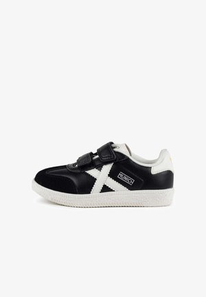 Zapatillas deportivas en blanco y negro con correas de velcro, materiales de cuero y ante, suela texturizada, con un diseño distintivo de estrella blanca y logotipo.
