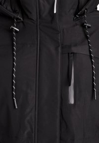 Crna vodonepropusna jakna s patentnim zatvaračem, podesivim utezima i glatkom teksturom. Ima kapu i minimalistički dizajn.