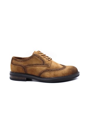 Chaussure habillée en daim beige avec des perforations décoratives et un bout en cuir lisse. Présentant un design à lacets et une semelle en caoutchouc noir basse.