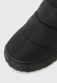Sort, polstret støvle med rund tå og tekstureret gummisål med dekorative mønstre. Glat tekstiloverdel med syede detaljer.