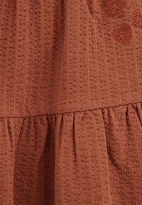 Robe en coton couleur rouille avec un motif texturé, présentant des plis froncés à l'ourlet et des accents de cœur brodés.