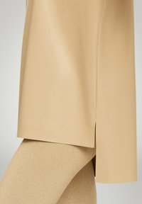 Nude high-shine tunic with side slits, paired with glittering gold leggings. The tunic has a smooth texture, while the leggings shimmer.