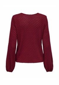 Maglione a maglia bordeaux con un motivo texture, scollatura rotonda e maniche lunghe a sbuffo. Il materiale appare morbido e leggero.