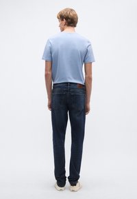 Ανοιχτό μπλε κοντομάνικη μπλούζα συνδυασμένη με σκούρο μπλε τζιν. Το τζιν διαθέτει πέντε τσέπες και ένα καφέ δερμάτινο ταμπελάκι στη μέση.