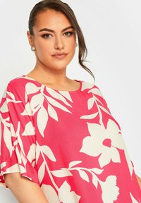 Top loose-fit di colore rosa con grandi motivi floreali bianchi e foglie, maniche corte e scollatura rotonda. Tessuto dalla texture liscia.