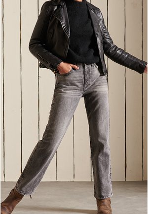 Zwarte leren jas, zwart gebreide trui en grijze jeans met rechte pijpen. Bruine enkellaarsjes, casual fit, met textuur en zichtbare stiksels.