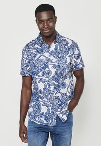 Camicia a maniche corte in cotone bianco con motivo floreale blu, dotata di colletto a camicia e tasca sul lato sinistro.