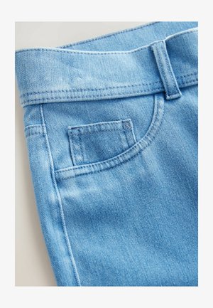Jean en denim bleu clair avec une ceinture, une petite poche avant et des détails de couture visibles. Le tissu a une texture lisse.