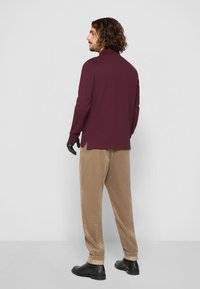 Burgunderfarvet langærmet top med høj krave, parret med beige kordfløjspants og sorte sko. Minimalistisk design, glat tekstur.