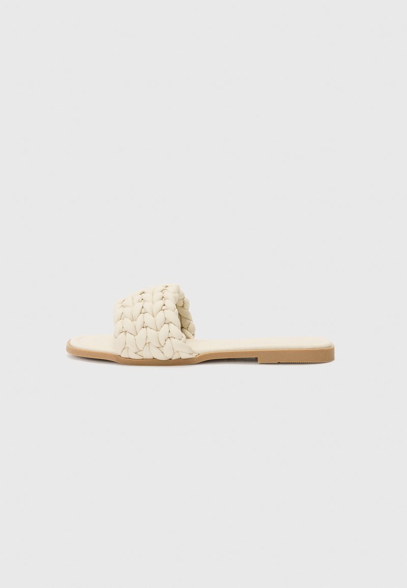Light beige flat sandals featuring a woven upper with a braided texture, and a minimalistic rubber sole. Simple and open design.
