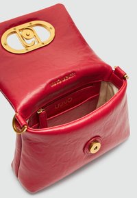 Rotene Lederhandtasche mit einem goldenen ovalen Hardwareverschluss, Innenfächern und einer glatten, strukturierten Oberfläche. Mit Markenprägung im Inneren.
