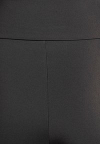 Leggings neri con una texture liscia ed elastica. Presentano una cintura alta e una cucitura che corre verticalmente sul davanti.