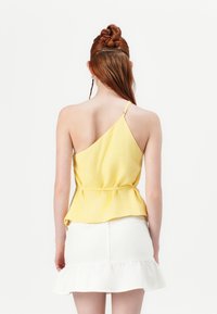 Asymmetrical yellow top made of lightweight fabric with a peplum waist, paired with a white ruffled mini skirt.