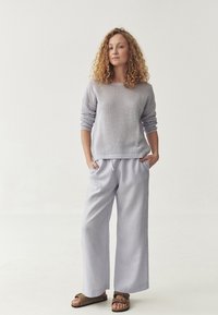 Maglione lavanda chiaro con un motivo a maglia testurizzato, abbinato a pantaloni larghi di un delicato colore lavanda. Sandali marroni completano il look.
